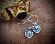 Silver skull-themed earrings on a wooden surface with gold and black decorative items.